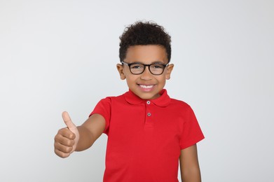 Photo of African-American boy with glasses showing thumb up on light grey background