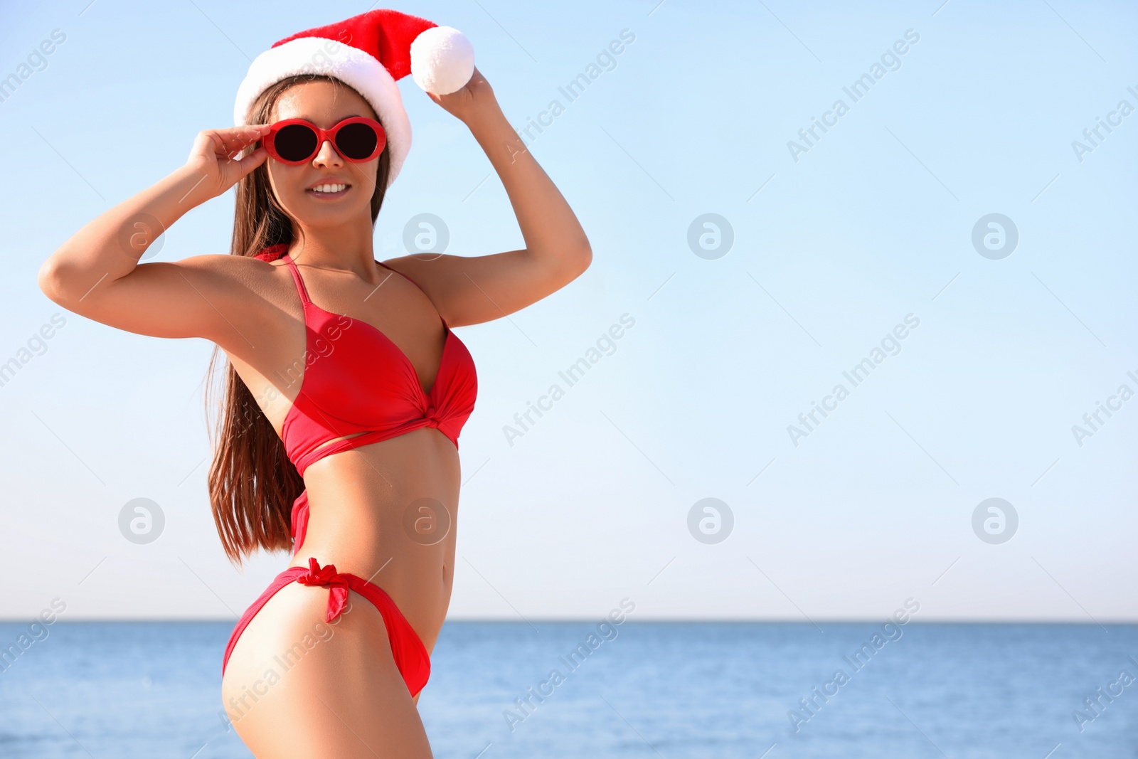 Photo of Beautiful young woman in Santa hat and bikini on beach, space for text. Christmas vacation