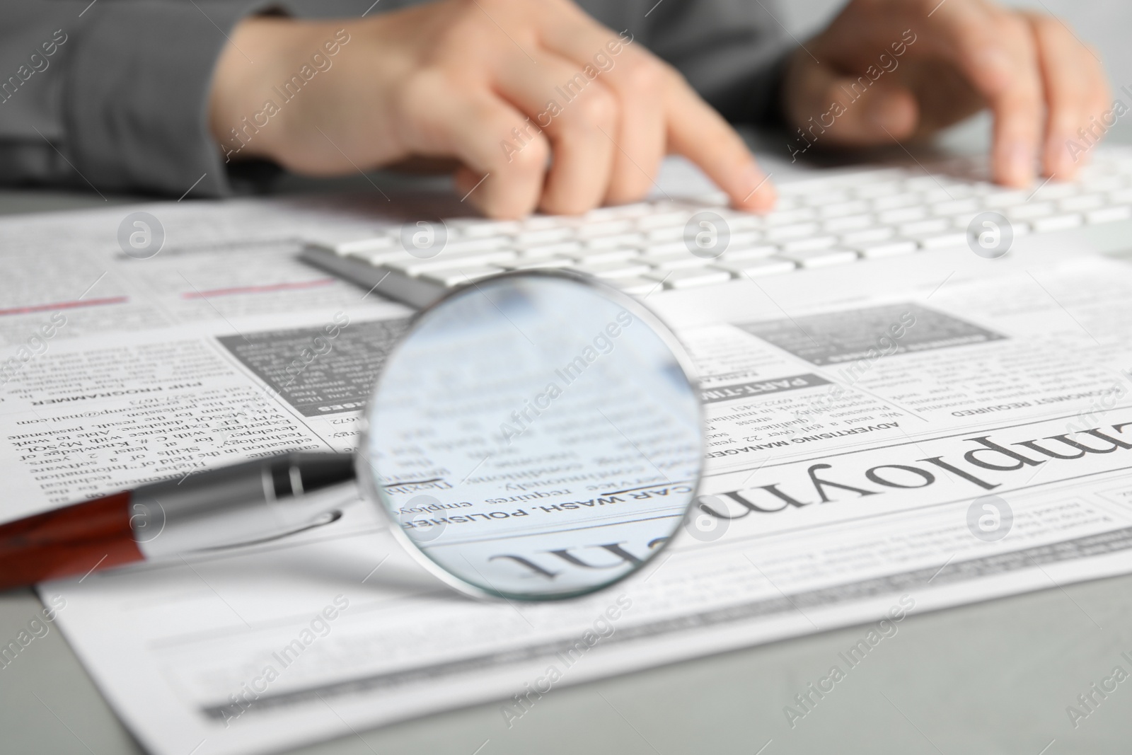 Photo of Looking through magnifying glass at newspaper and woman on background, closeup. Job search concept