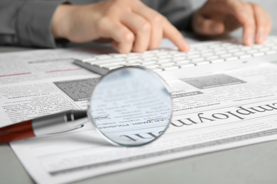 Photo of Looking through magnifying glass at newspaper and woman on background, closeup. Job search concept