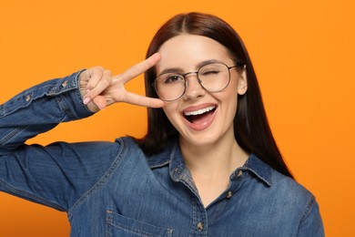 Portrait of woman in stylish eyeglasses gesturing on orange background