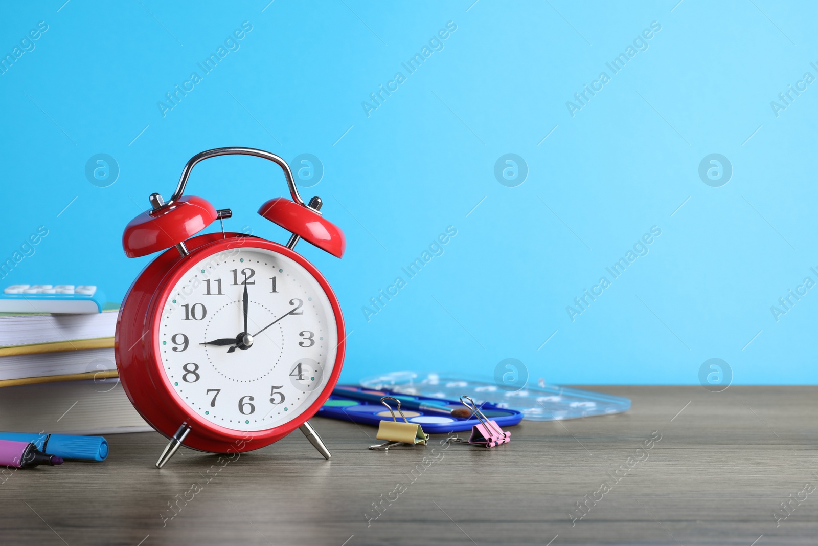 Photo of Red alarm clock and different stationery on wooden table against light blue background, space for text. School time