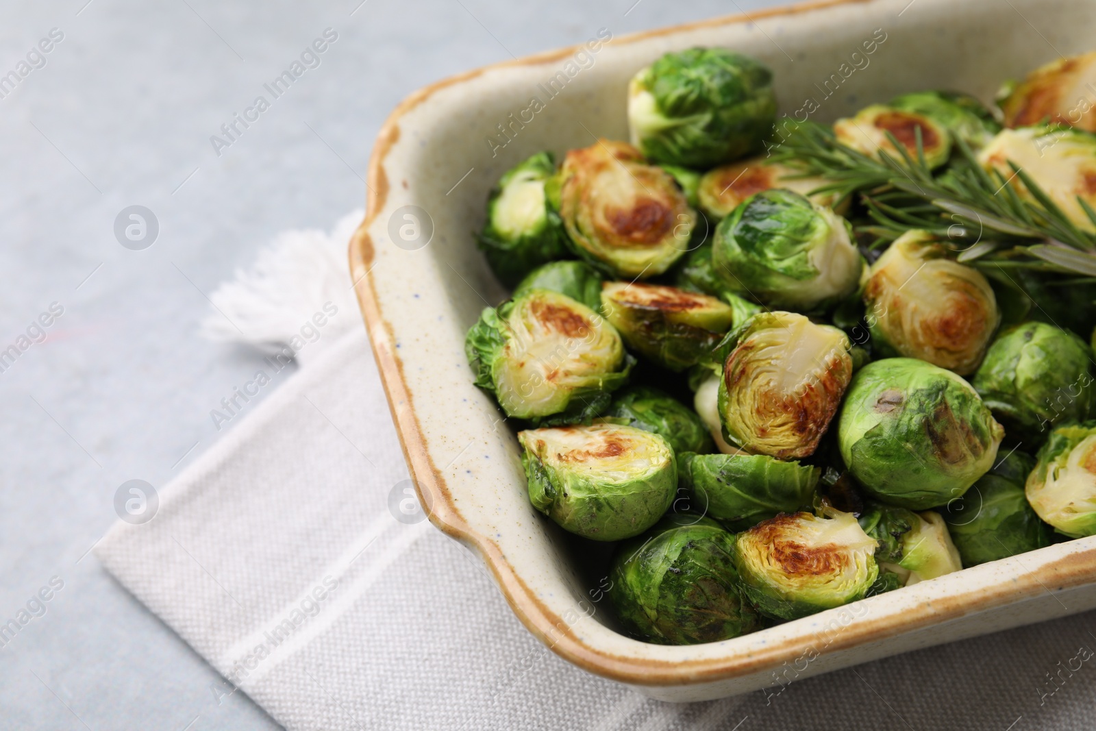 Photo of Delicious roasted Brussels sprouts and rosemary in baking dish on grey table, closeup. Space for text