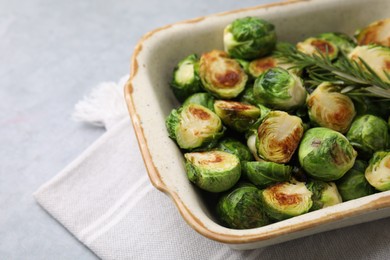 Photo of Delicious roasted Brussels sprouts and rosemary in baking dish on grey table, closeup. Space for text