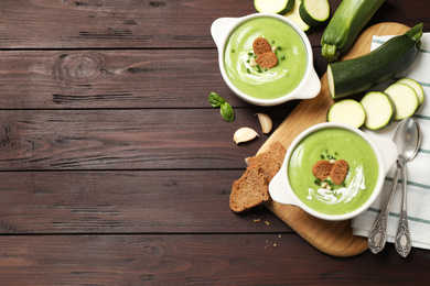 Photo of Tasty homemade zucchini cream soup served on wooden table, flat lay. Space for text