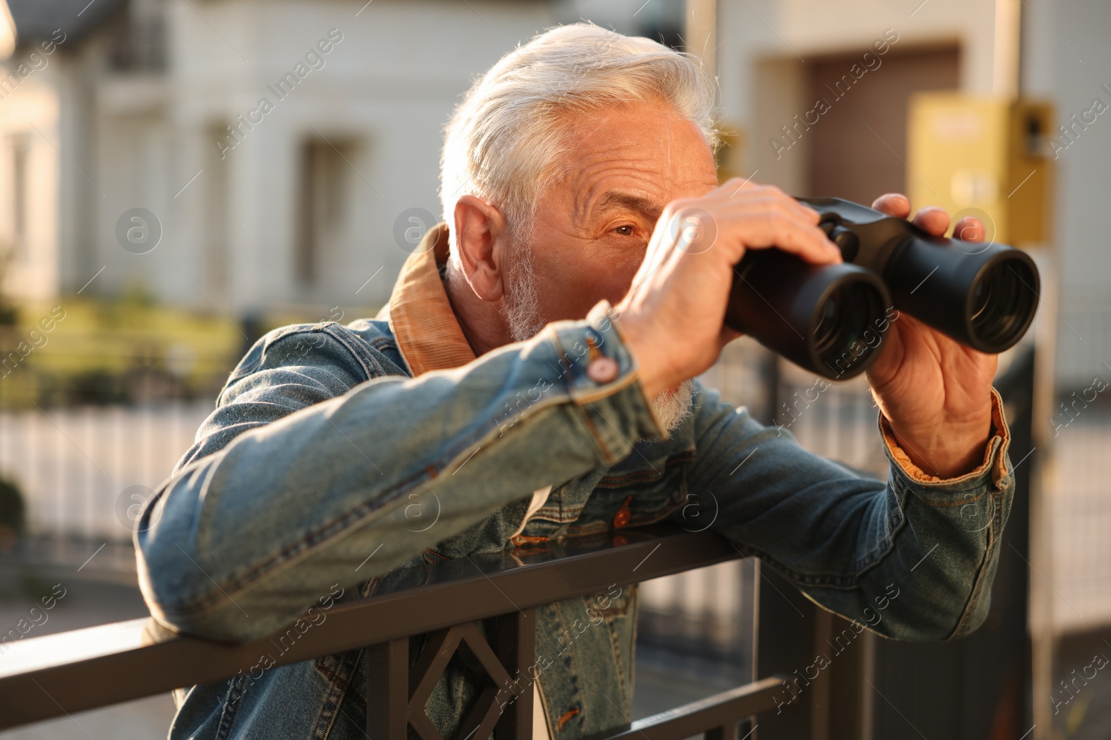 Photo of Concept of private life. Curious senior man with binoculars spying on neighbours over fence outdoors