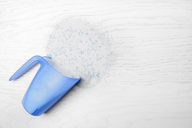 Measuring cup with laundry detergent on white wooden background, top view. Space for text