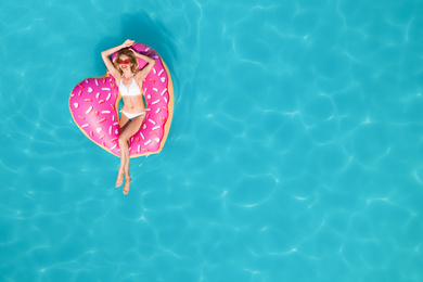 Young happy woman with inflatable ring in swimming pool, top view and space for text. Summer vacation