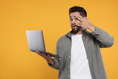 Embarrassed man holding laptop on orange background. Space for text