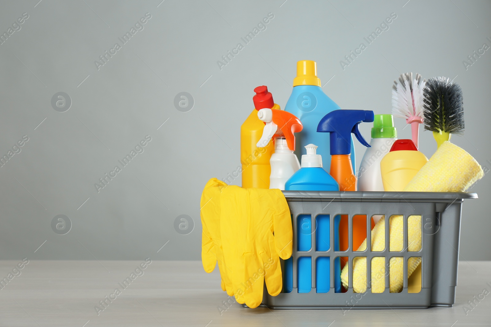 Photo of Basket with different cleaning products and supplies on light table. Space for text