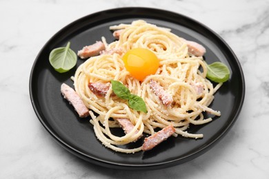 Photo of Plate of tasty pasta Carbonara with basil leaves on white marble table