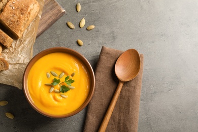 Flat lay composition with pumpkin cream soup in bowl on gray background. Space for text