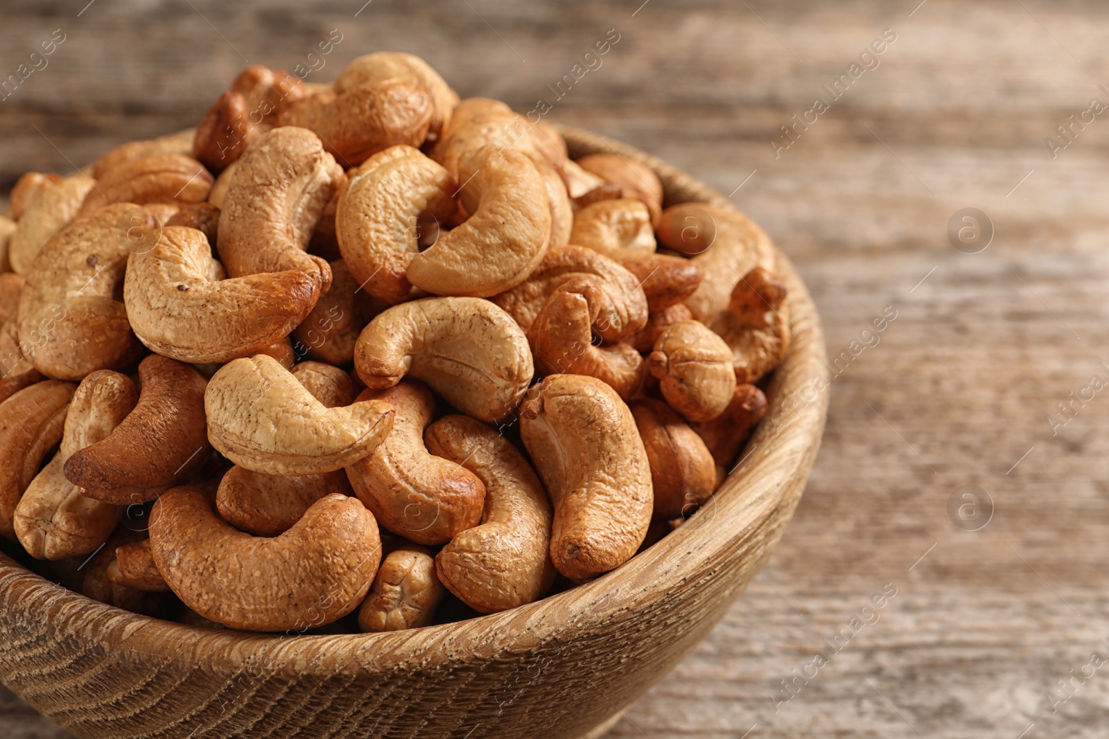 Photo of Tasty cashew nuts in bowl on wooden table, closeup. Space for text