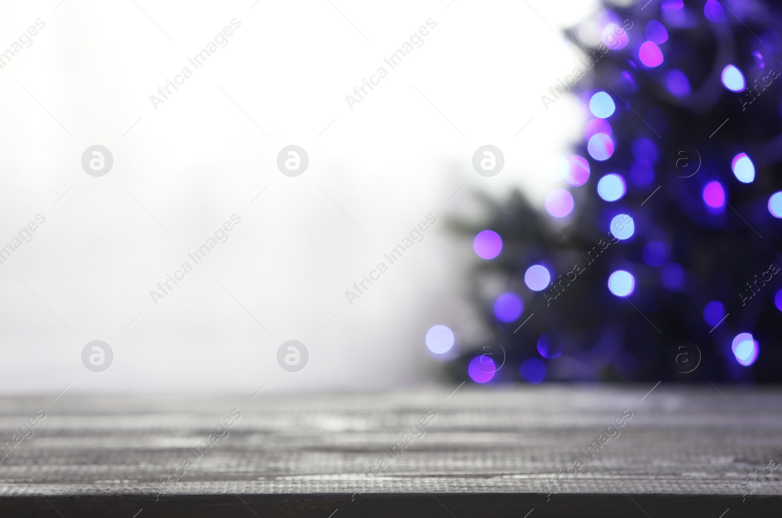 Photo of Empty table and blurred fir tree with violet Christmas lights on background, bokeh effect. Space for design