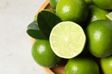 Photo of Fresh ripe limes and green leaves on light table, top view. Space for text