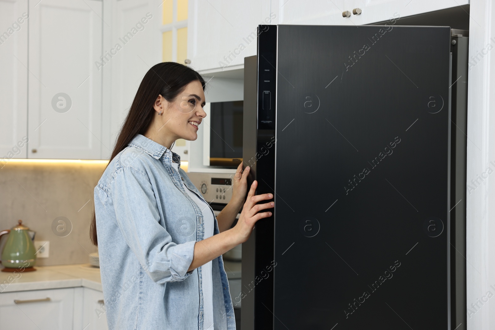 Photo of Young woman near modern refrigerator in kitchen