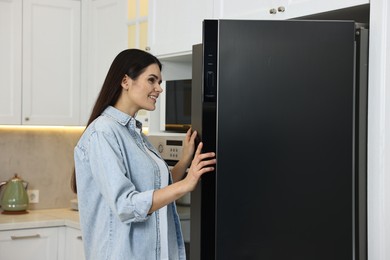 Photo of Young woman near modern refrigerator in kitchen