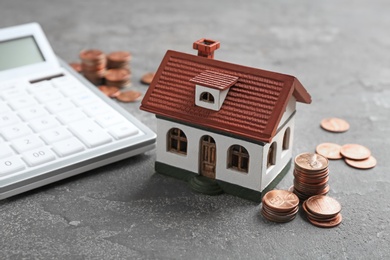 Photo of House model, coins and calculator on grey background