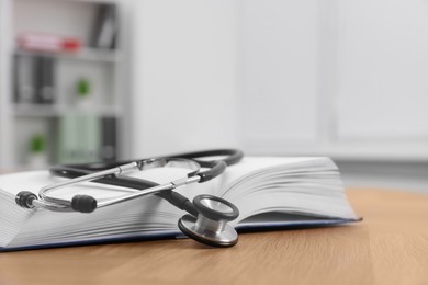 Photo of Book and stethoscope on wooden table in clinic. Space for text