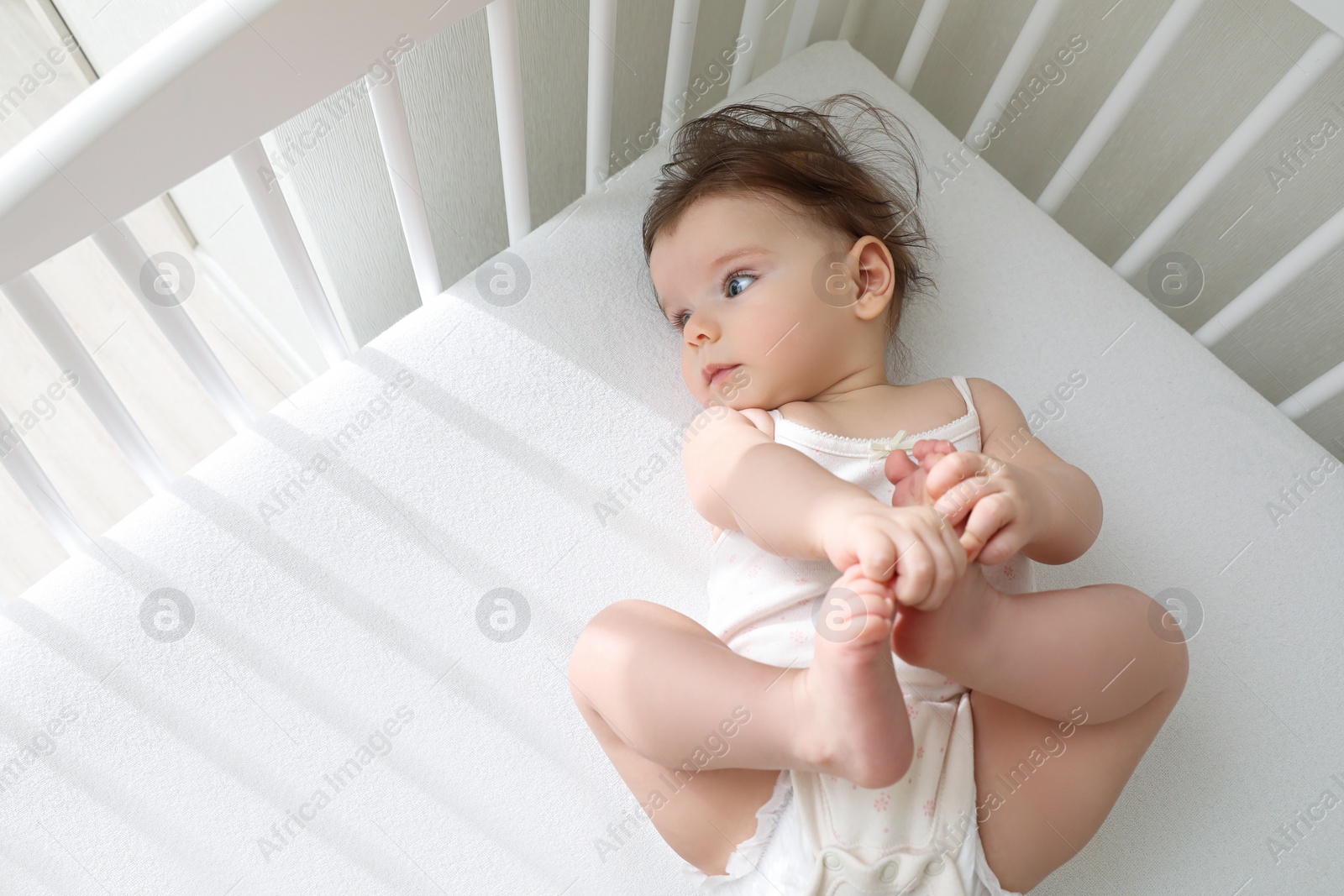 Photo of Cute little baby lying in comfortable crib at home, above view