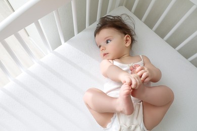 Cute little baby lying in comfortable crib at home, above view