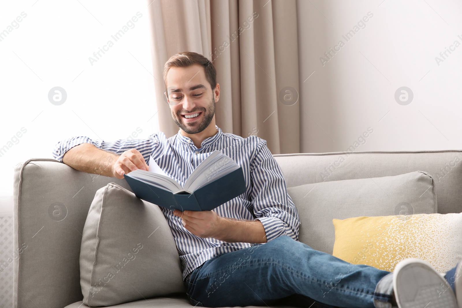 Photo of Handsome young man reading book on sofa at home