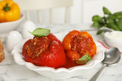 Photo of Delicious stuffed peppers with basil in bowl on white marble table