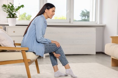 Photo of Woman suffering from leg pain on armchair at home