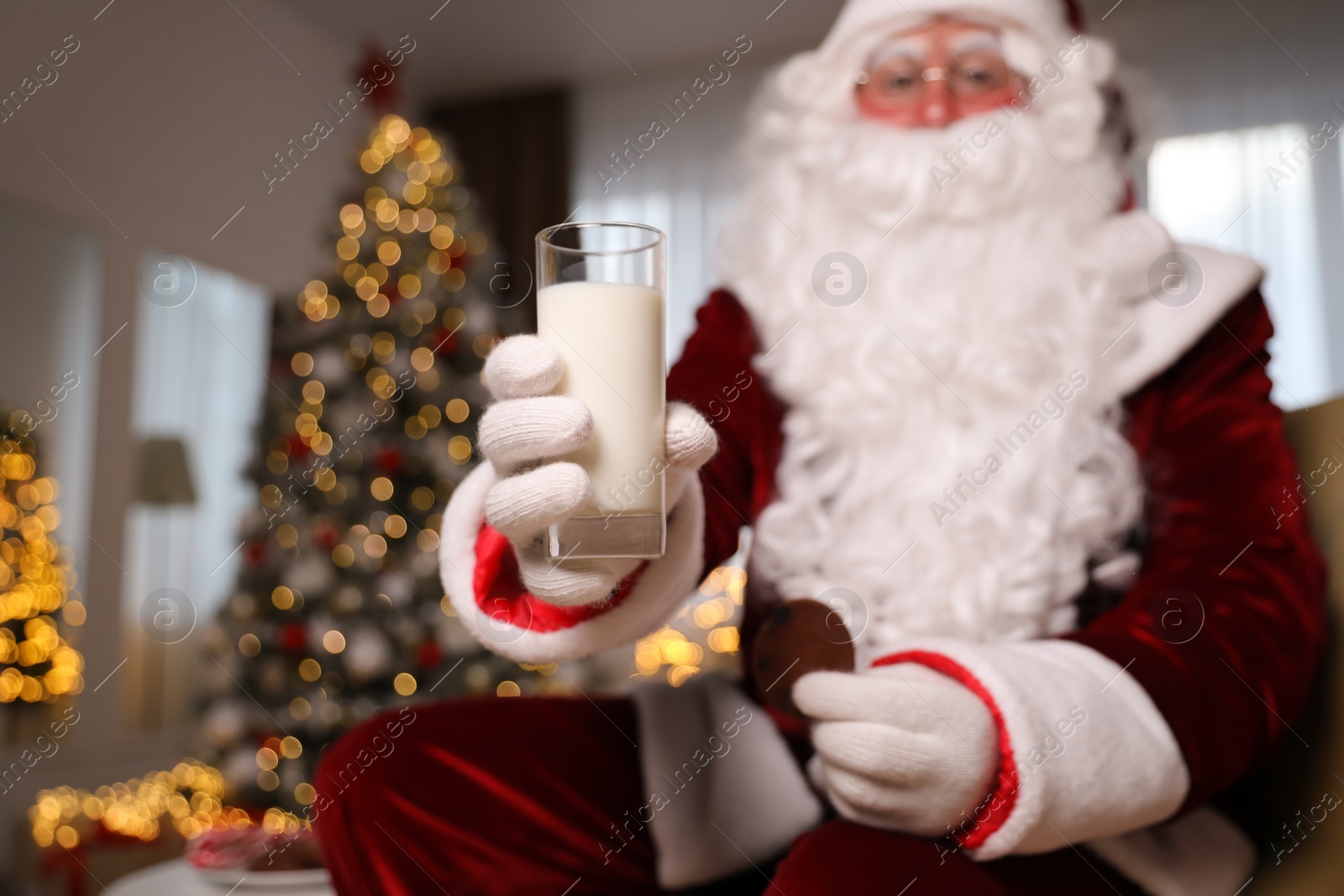 Photo of Santa Claus in room decorated for Christmas, focus on glass of milk