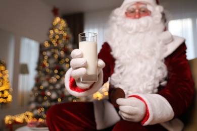 Photo of Santa Claus in room decorated for Christmas, focus on glass of milk