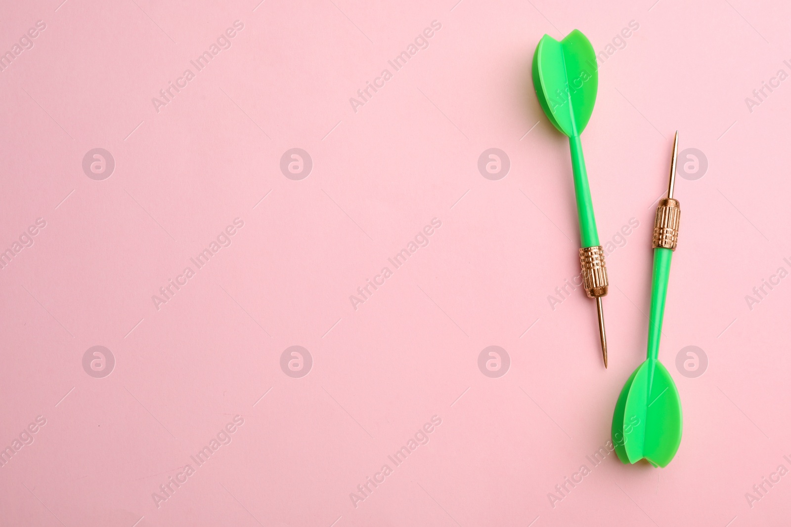 Photo of Green dart arrows on pink background, flat lay with space for text