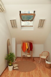 Stylish clothes rack, mirror and wicker chair in attic room. Interior design