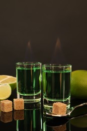 Photo of Flaming absinthe in shot glasses, brown sugar, lime and spoon on mirror table. Alcoholic drink