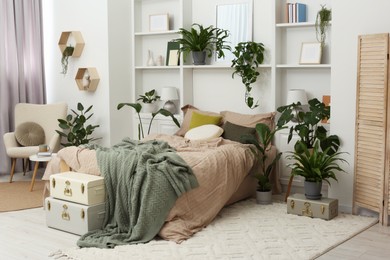 Stylish bedroom with comfortable bed and different houseplants. Interior design