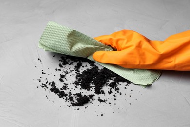 Photo of Woman in glove sweeping scattered coffee grounds with paper towel from light table, closeup