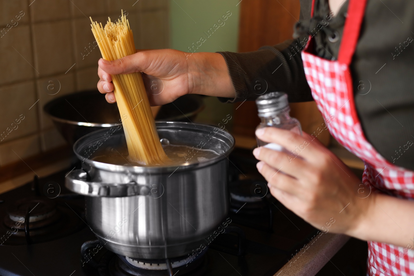 Photo of Woman cooking spaghetti on stove in kitchen, closeup