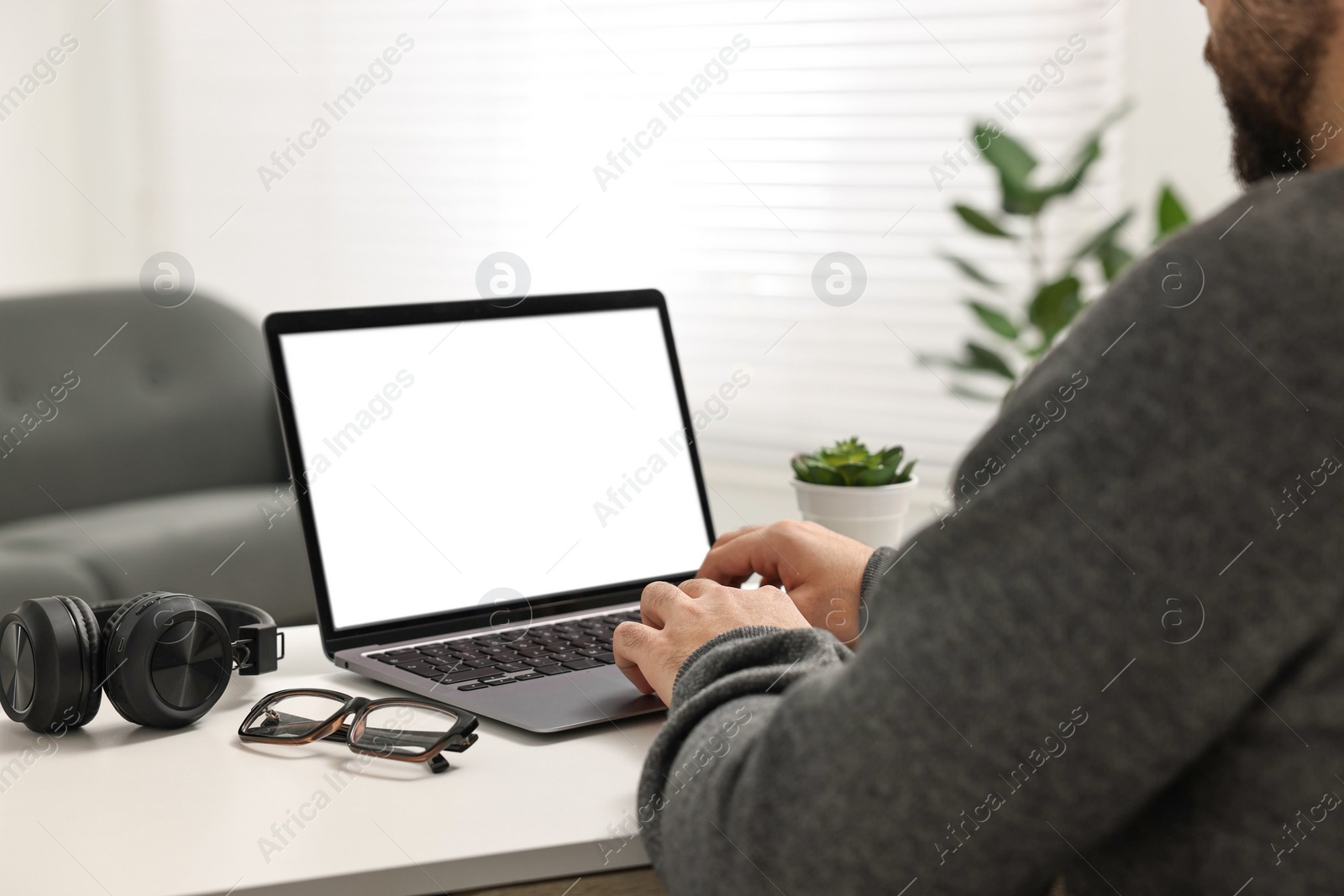 Photo of E-learning. Young man using laptop at white table indoors, closeup