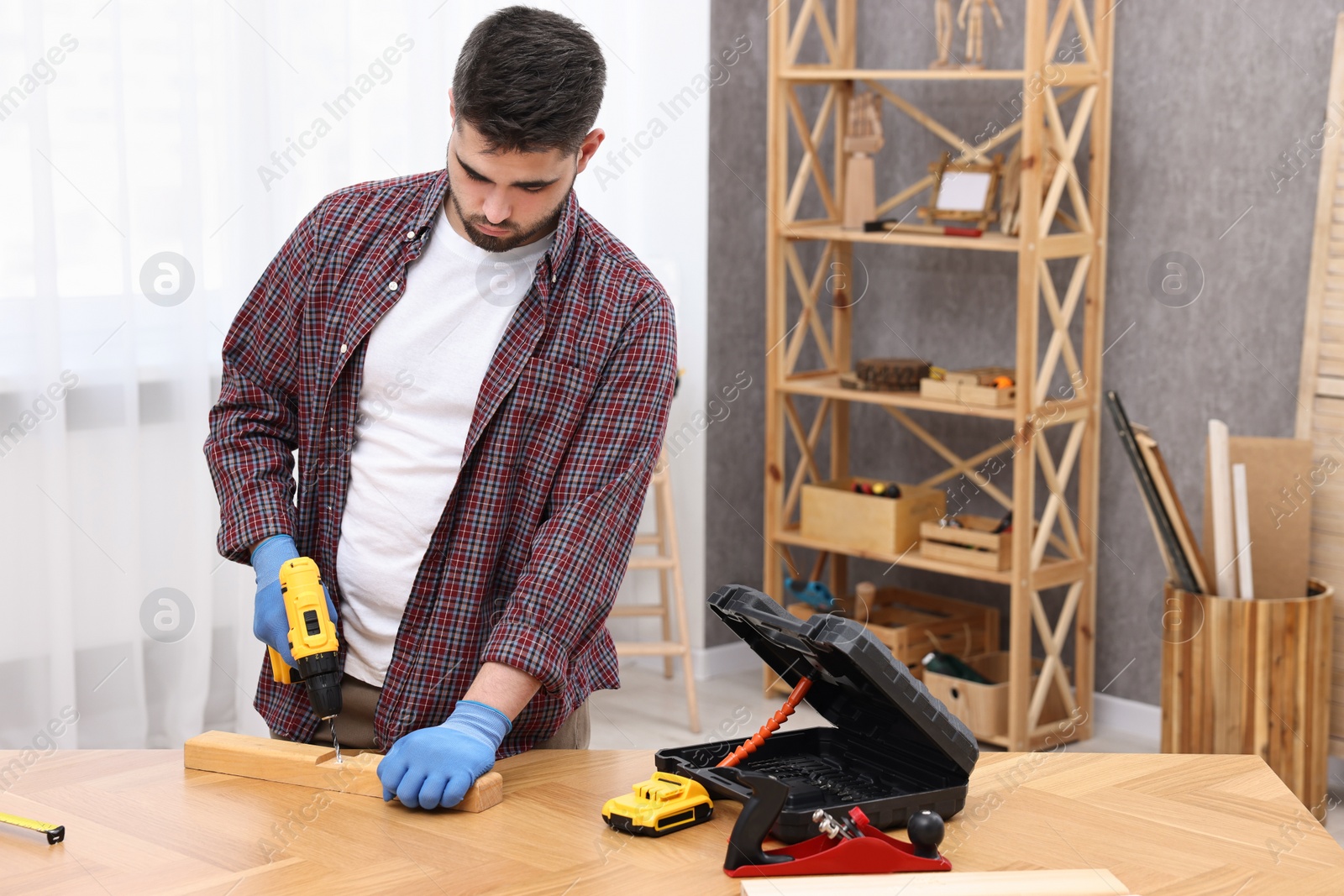Photo of Young handyman working with electric drill at table in workshop