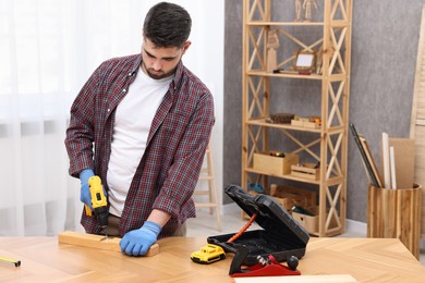 Young handyman working with electric drill at table in workshop