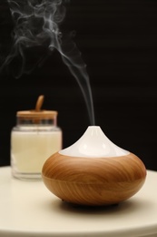 Photo of Aroma oil diffuser on table near black wall