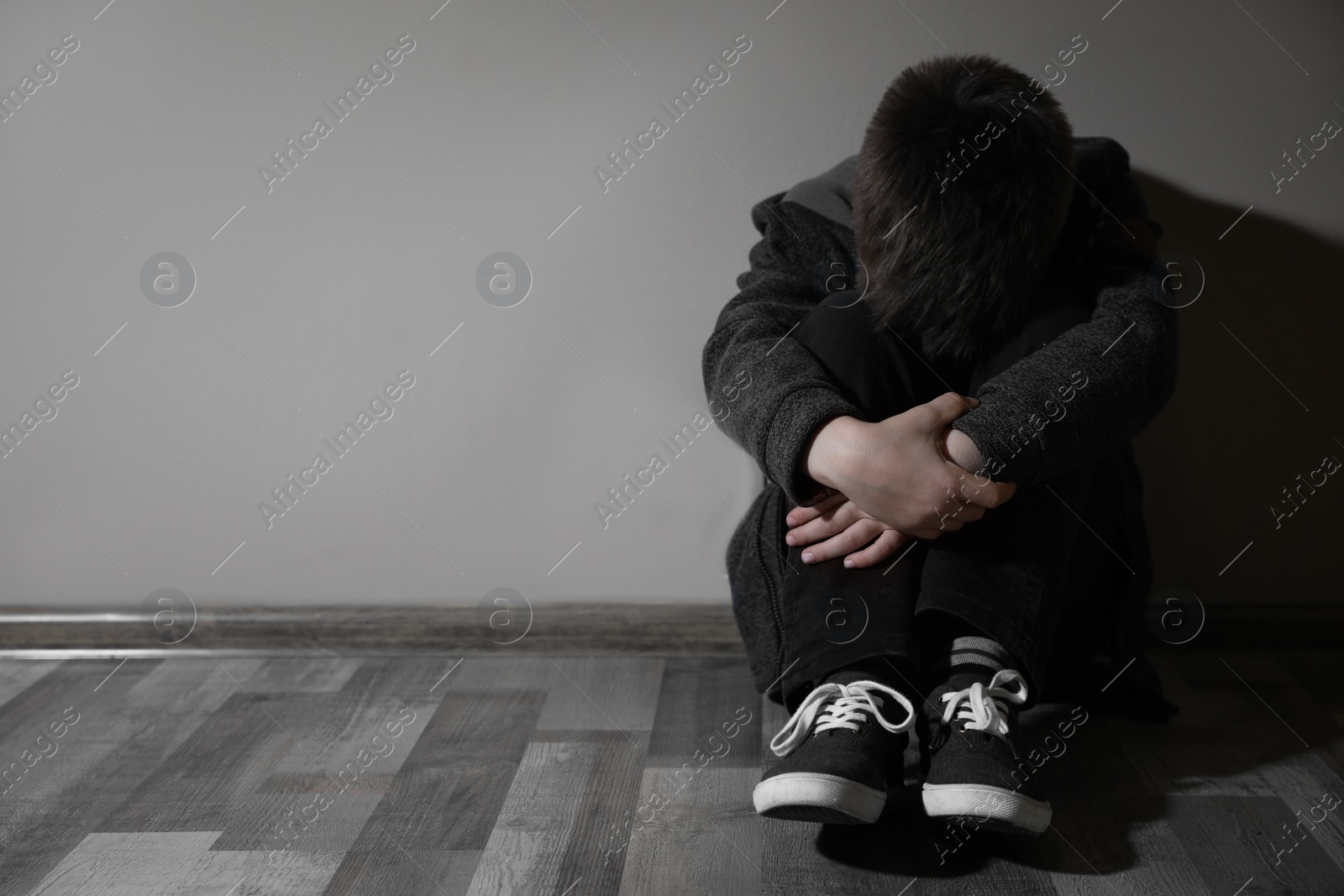 Photo of Scared little boy near beige wall, space for text. Domestic violence concept