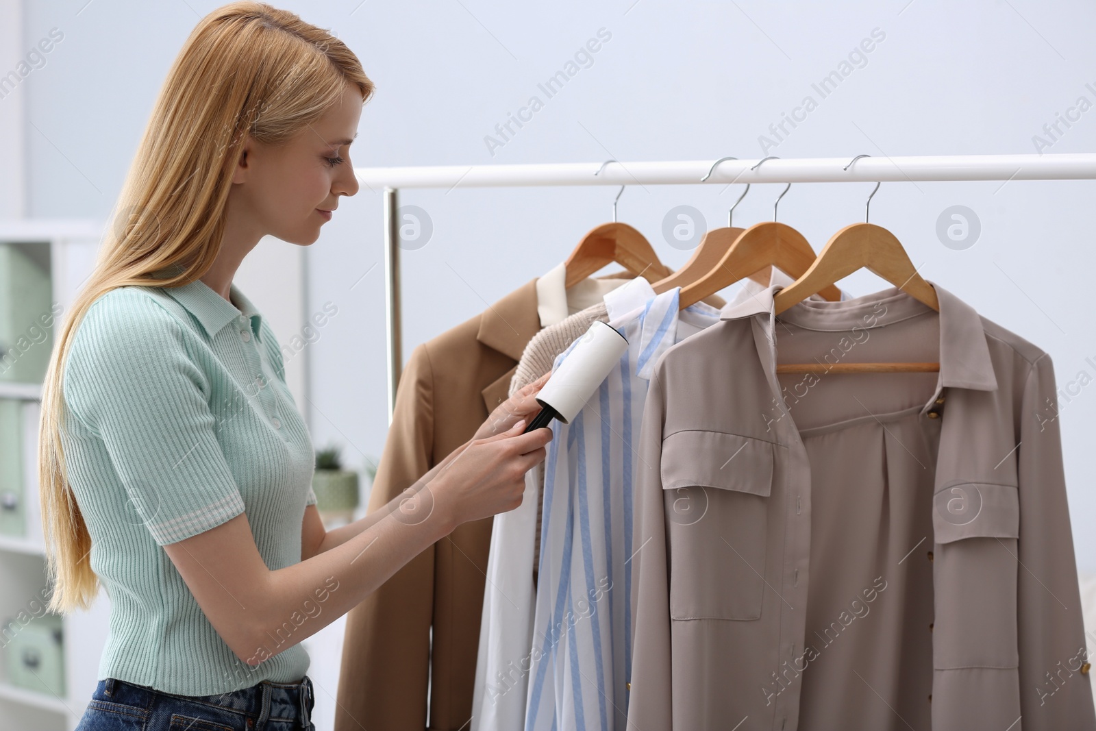 Photo of Young woman cleaning clothes with lint roller indoors