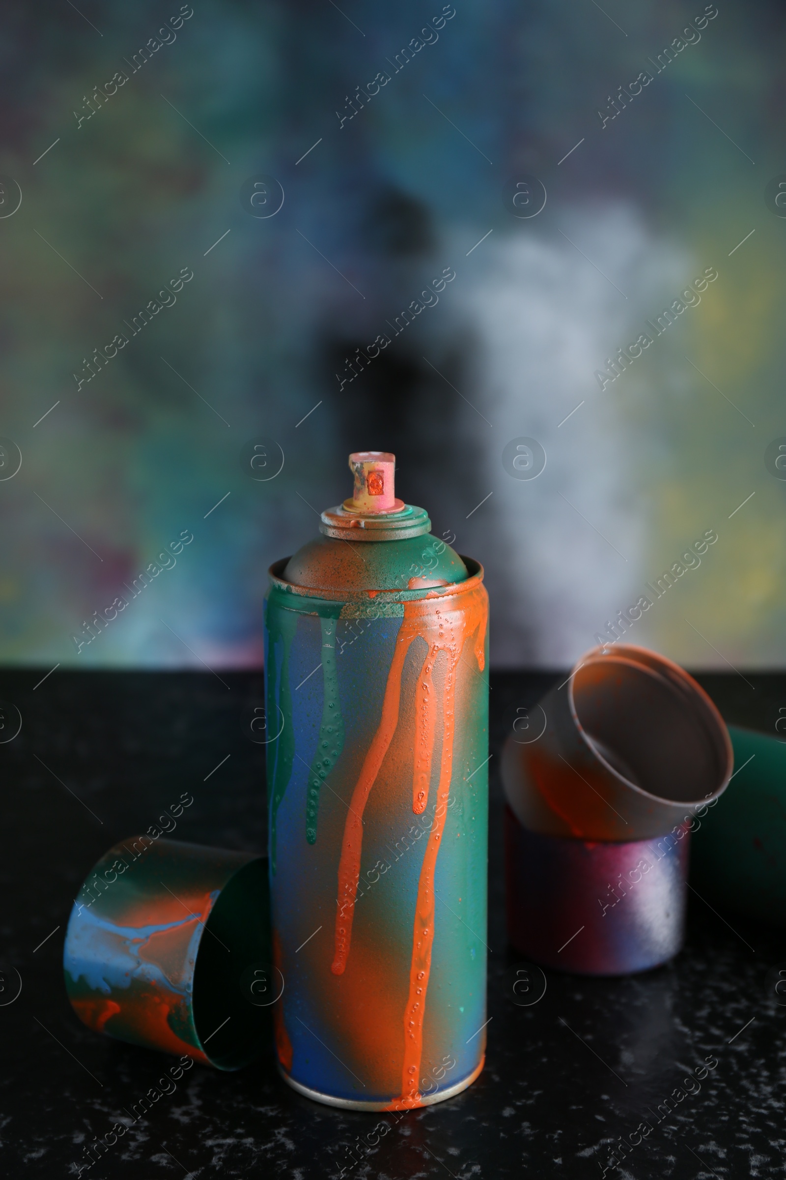 Photo of Spray paint can and caps on black textured surface against color background