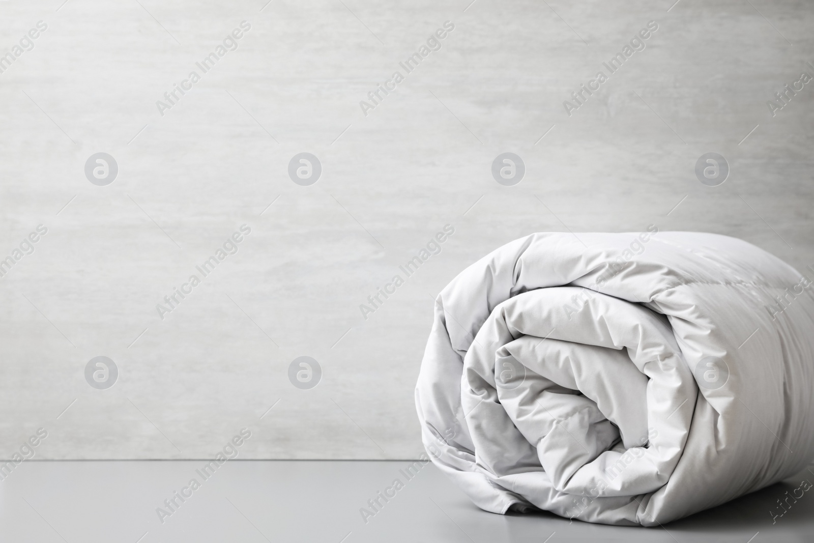 Photo of Soft rolled blanket on light grey table. Space for text