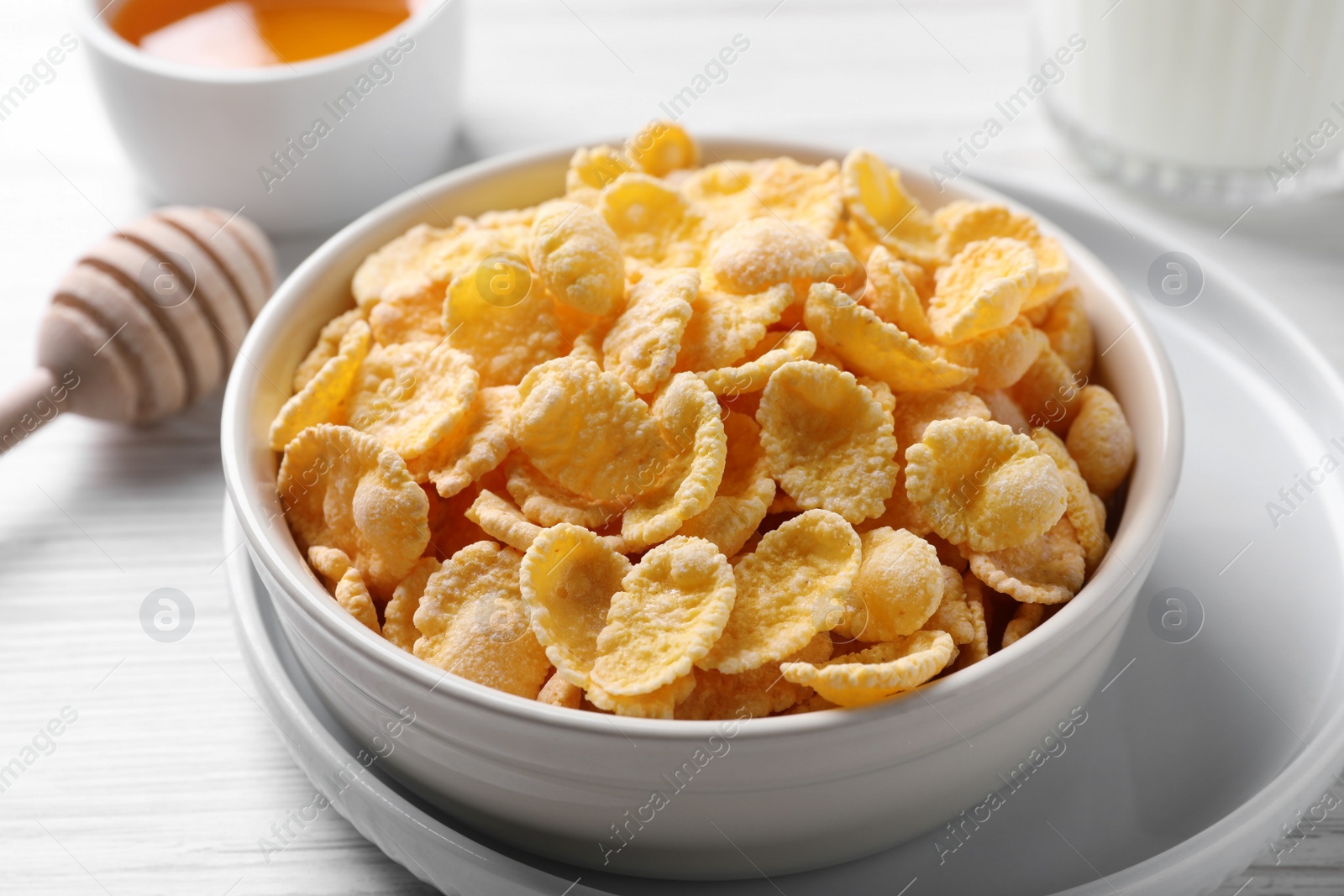 Photo of Bowl of tasty crispy corn flakes on white wooden table, closeup