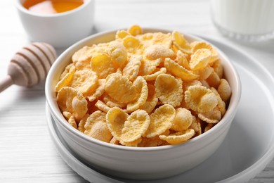 Photo of Bowl of tasty crispy corn flakes on white wooden table, closeup