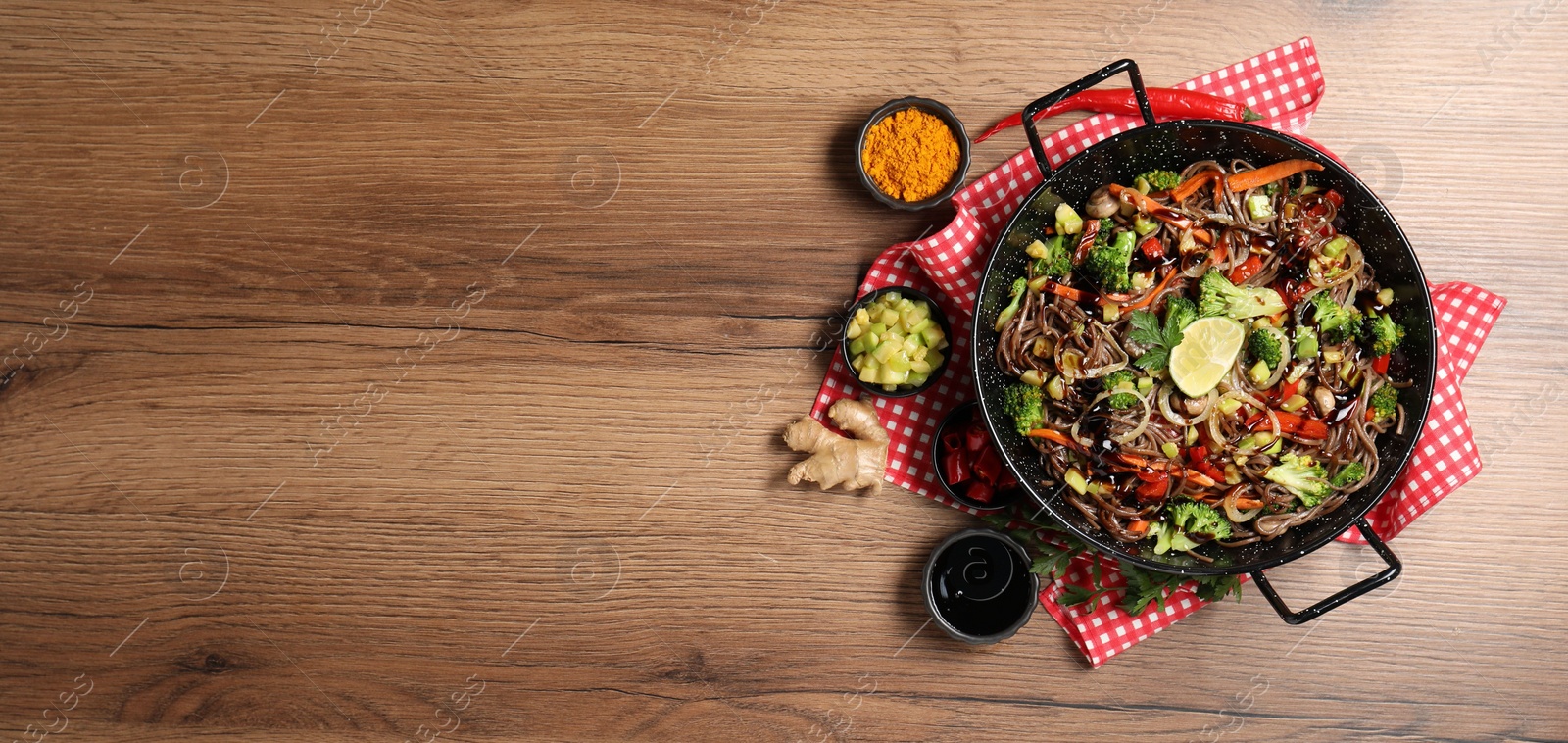 Photo of Stir-fry. Tasty noodles with meat in wok and ingredients on wooden table, flat lay. Space for text