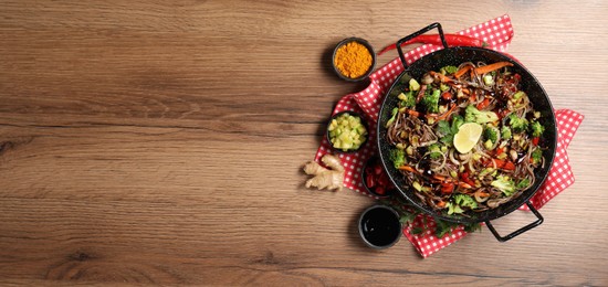 Photo of Stir-fry. Tasty noodles with meat in wok and ingredients on wooden table, flat lay. Space for text