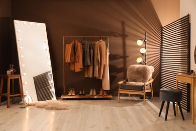 Photo of Stylish mirror with light bulbs and comfortable armchair in dressing room. Interior design