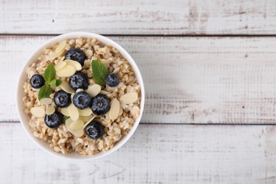 Photo of Tasty oatmeal with blueberries, mint and almond petals in bowl on white wooden table, top view. Space for text